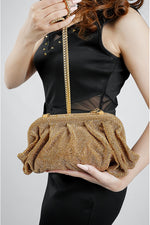 Gold rhinestone mesh clutch bag held at the waist with a black dress