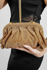 Gold Benedetta clutch bag held in front with the chain hanging, black outfit