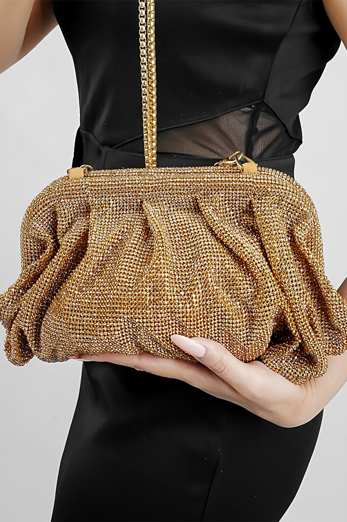 Gold Benedetta clutch bag held in front with the chain hanging, black outfit