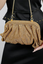 Woman holding a gold Benedetta clutch bag with the chain over her arm