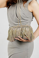 Woman holding a shimmer clutch bag in front with a grey dress