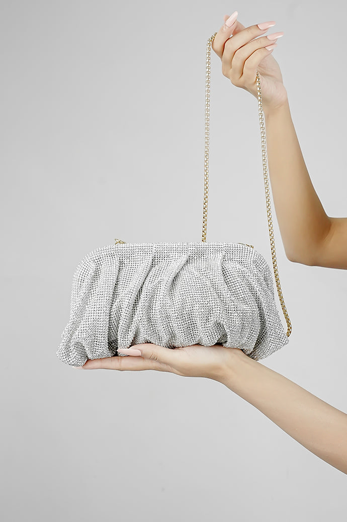 Silver rhinestone clutch bag resting in the hand against a grey background