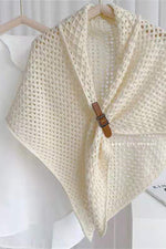 Bohemian open-knit winter cape for women in cream with a tan toggle fastener, on a hanger