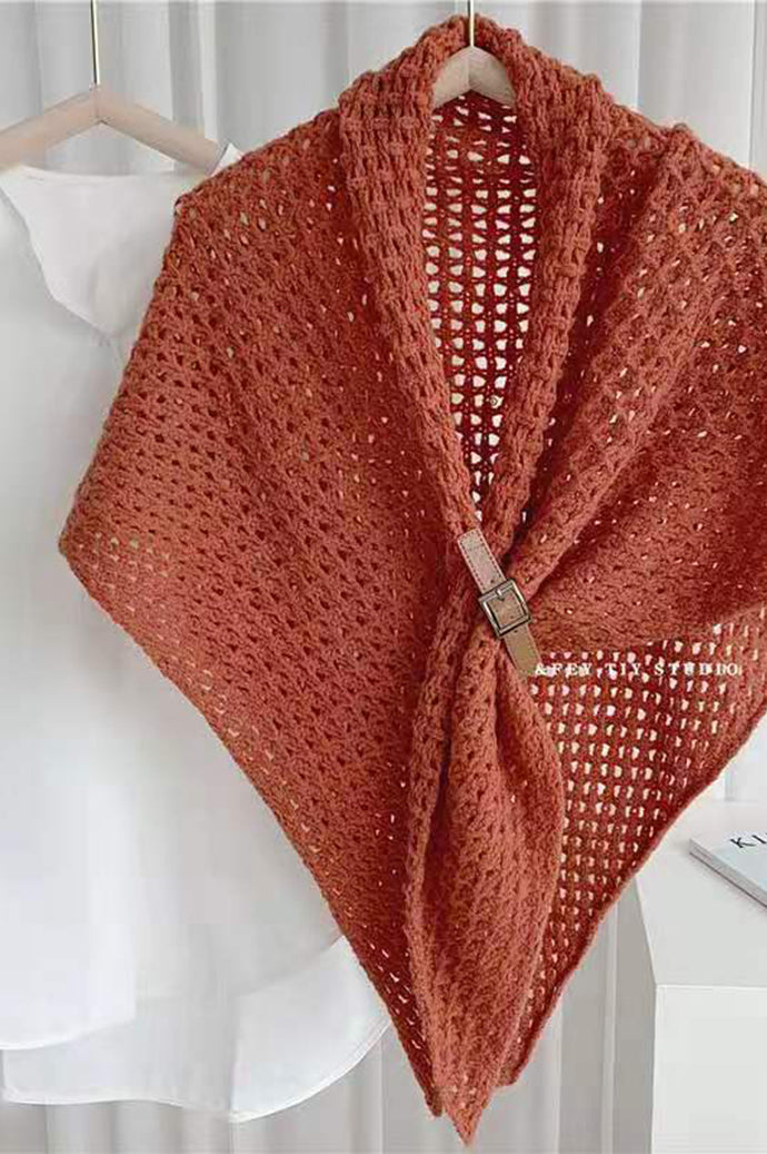Bohemian open-knit winter cape for women in rust orange with a tan toggle fastener, on a hanger