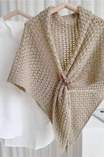Bohemian open-knit winter cape for women in taupe with a tan toggle fastener, on a hanger