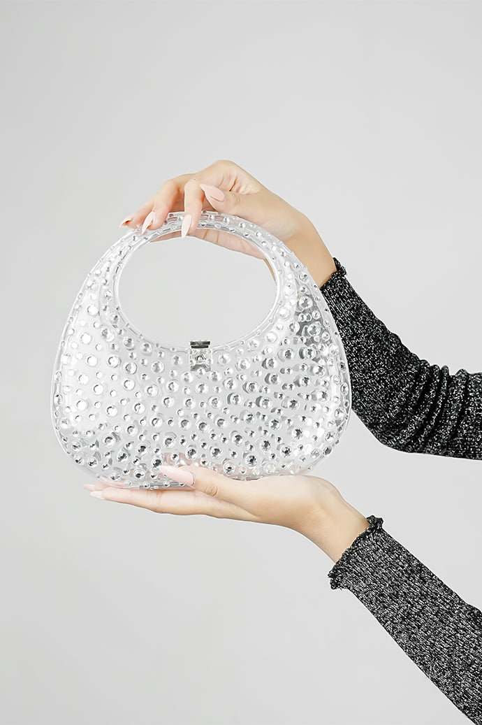 Clear clutch bag held with both hands, showing the handle and clasp