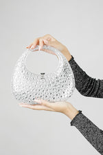 Clear clutch bag held with both hands, showing the handle and clasp