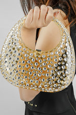 Close-up of a gold textured clutch bag held up by the handle