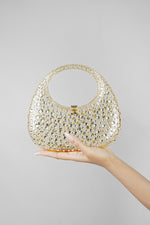 Gold clutch bag held in the hand against a plain grey background