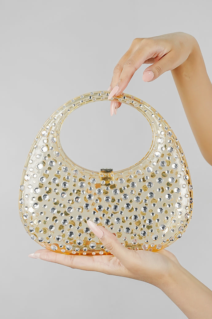 Gold clutch bag held by the handle with one hand, angled view