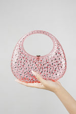 Pink clutch bag for women held in the hand against a plain background