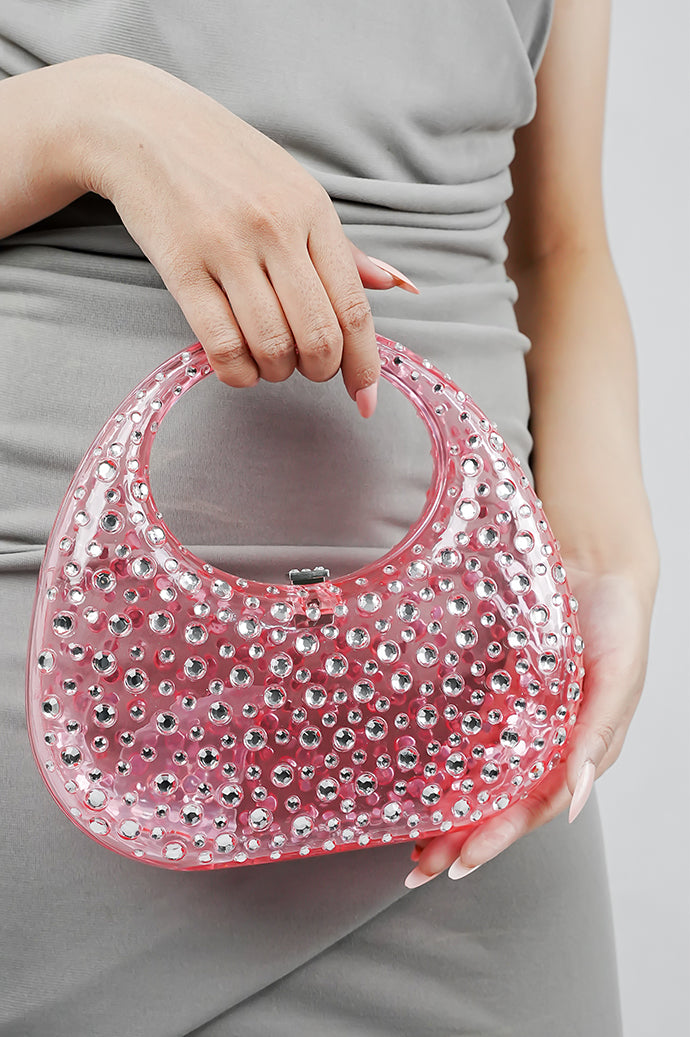 Woman holding a pink clutch bag at her waist, full outfit view