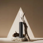 Black commercial aroma diffuser on a stone slab with driftwood releasing a thin mist