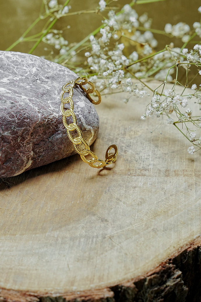 Gold chain-link open bangle resting on a wooden slice
