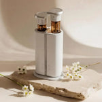 Dual scent aroma diffuser with two amber bottles on a stone slab beside white daisies