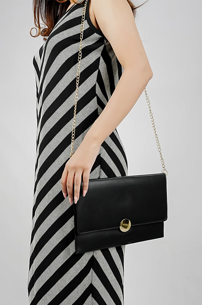 Black Envelope Bag hanging from a gold chain with a striped dress