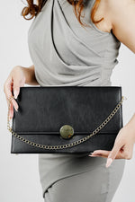 Black Envelope Bag for women with gold emblem and chain held in front, Future Style Pakistan