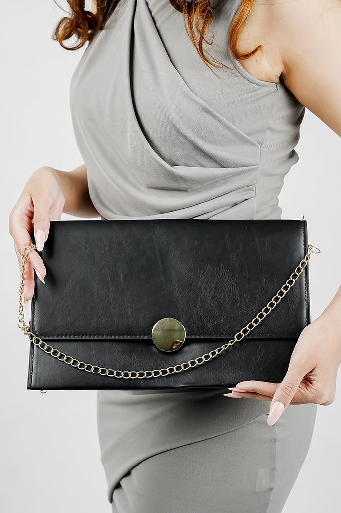 Black Envelope Bag for women with gold emblem and chain held in front, Future Style Pakistan