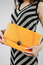 Orange Envelope Bag held in both hands with a striped dress