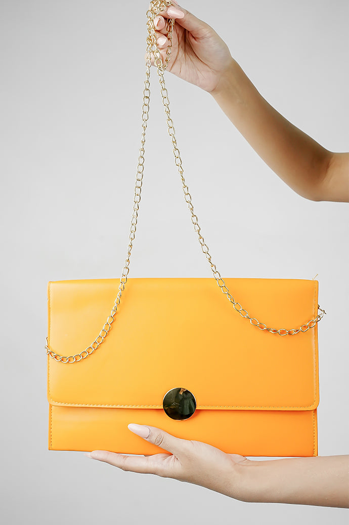 Orange Envelope Bag with gold chain held up on a grey background
