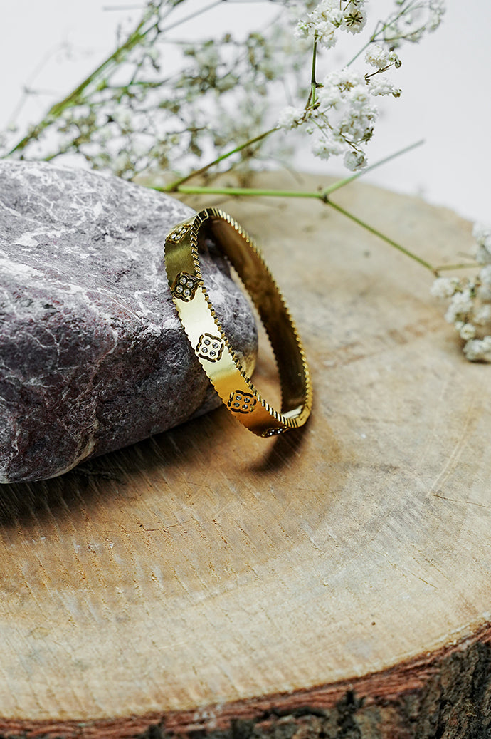 Gold-tone clover bangle standing on a wood slice, side view