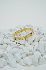 Gold-tone clover bangle with stone accents displayed on white stones