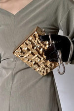 Gold hammered clutch for women held in front, styled with a V-neck grey dress