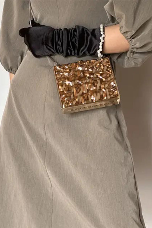 Gold rectangle clutch with hammered effect held at the waist with black gloves, Future Style Pakistan