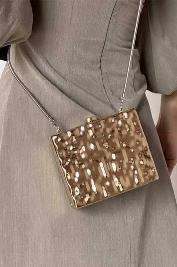 Woman holding the gold hammered clutch with a grey dress and black satin gloves