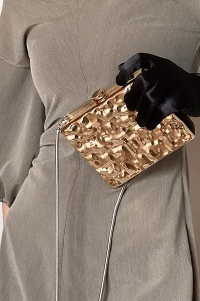 Gold hammered clutch with clasp carried in hand, side view