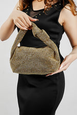 Woman holding the Hubo gold clutch with knotted handle against a black outfit