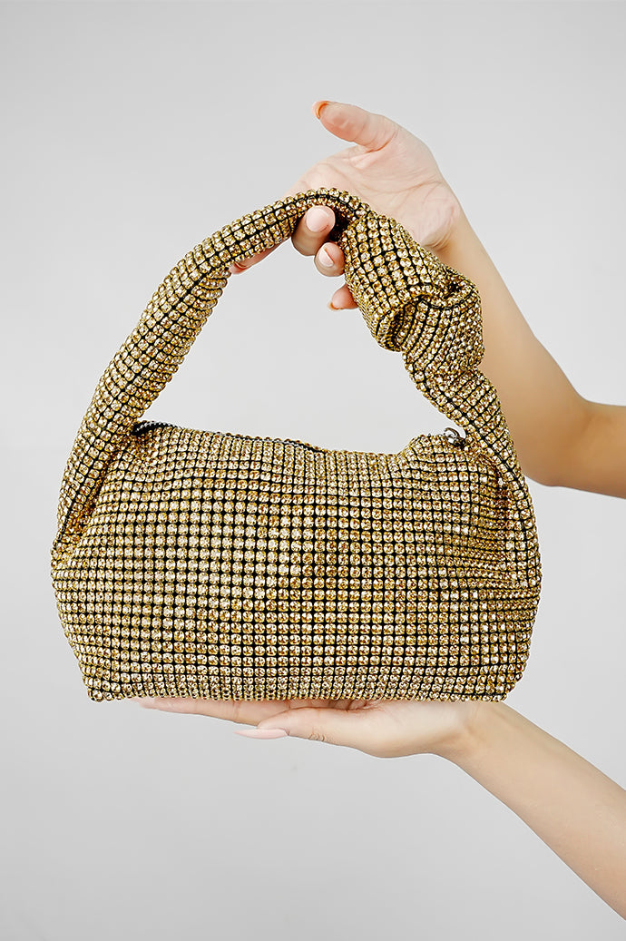 Hubo gold clutch with knot handle held in hand on a grey background