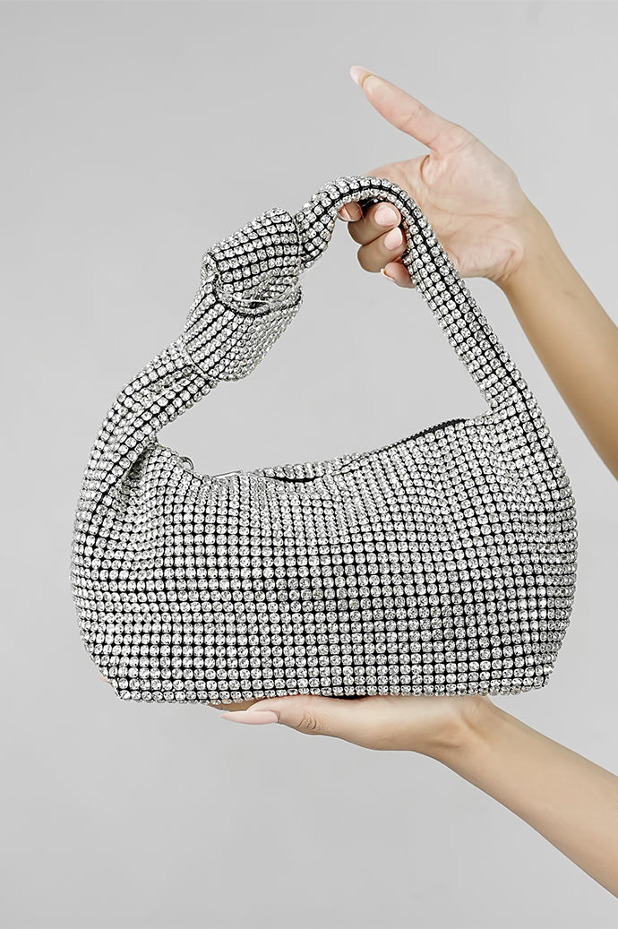 Hubo silver clutch with knotted handle held in hands on a grey background