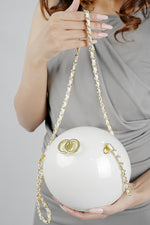 Woman in a grey dress holding the Luna white globe clutch by its chain