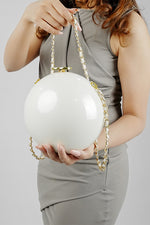 Woman holding the Luna white globe clutch by its gold chain