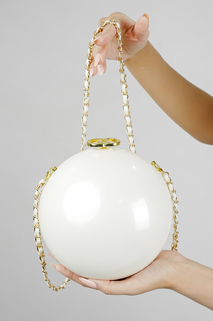 Luna white globe clutch with gold chain held in hands on a grey background