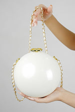 Luna white globe clutch with gold chain held in hands on a grey background