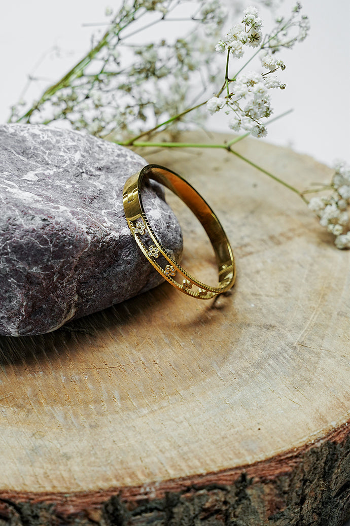 Gold open bangle with clove motifs standing on a wooden slice