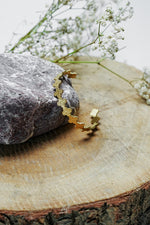 Gold open bangle with textured scalloped design on a wooden slice