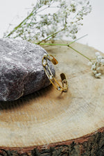 Gold open bangle with pearl details standing on a wooden slice