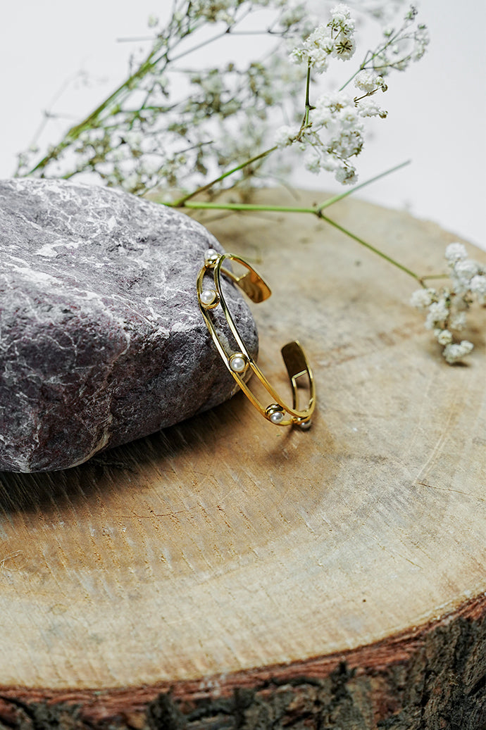 Gold open bangle with pearl details standing on a wooden slice