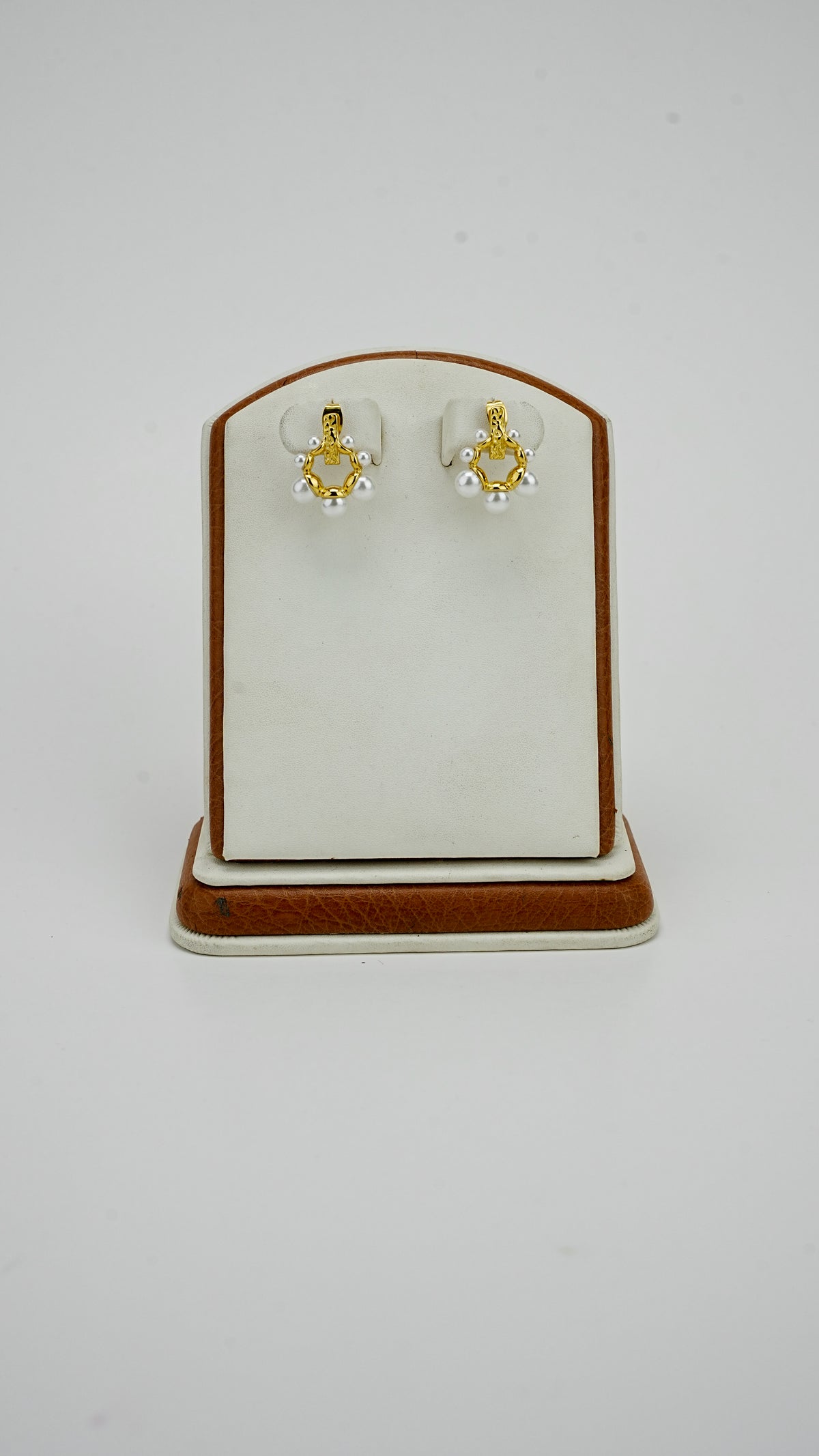 Gold earrings with pearl details for women on a display stand