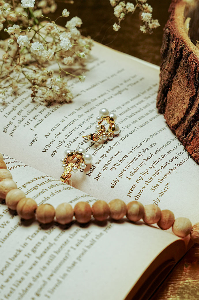 Gold pearl earrings on an open book with dried flowers and prayer beads