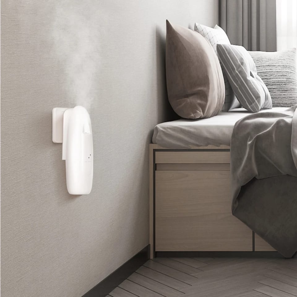 Plug-in aroma diffuser releasing mist on a living-room wall beside a table lamp