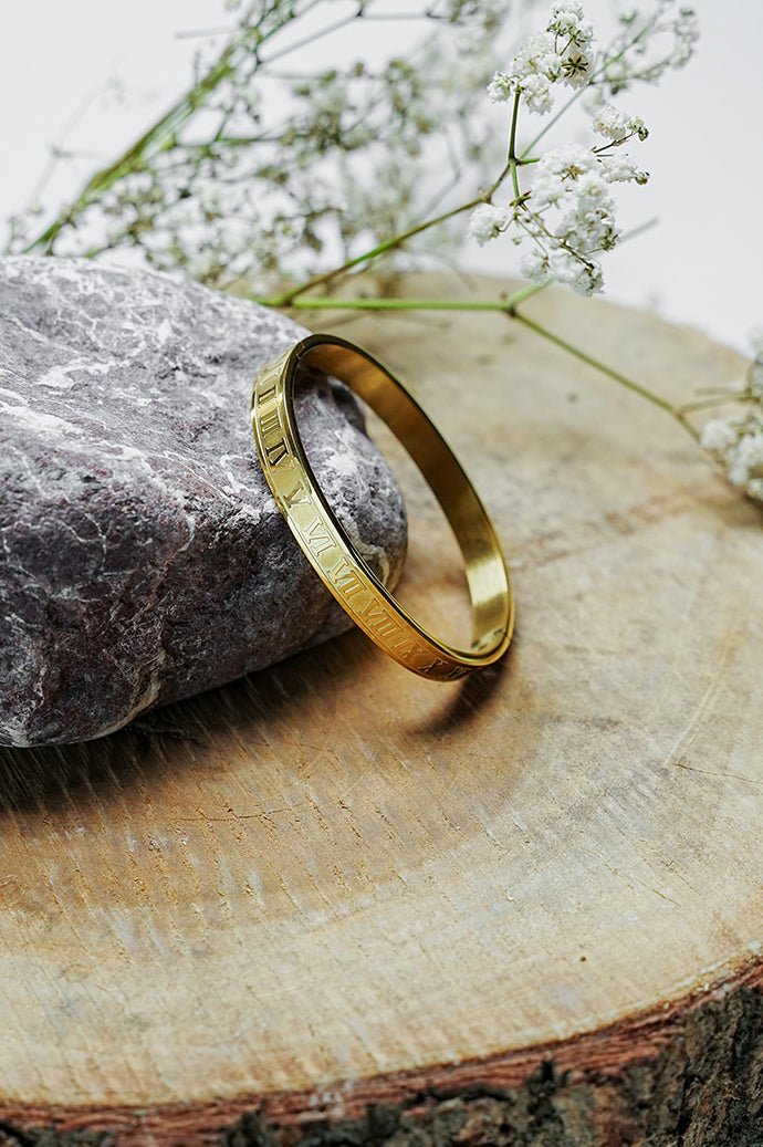 Gold close bangle with Roman numeral engraving standing on a wooden slice