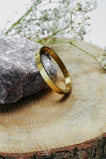 Gold close bangle with Roman numeral engraving standing on a wooden slice