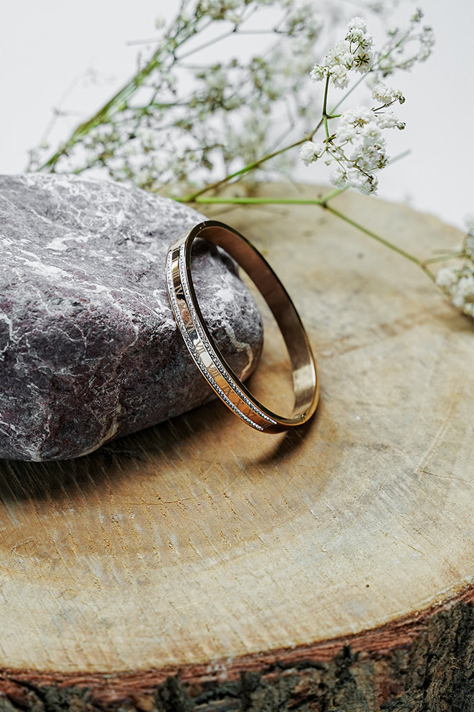 Side view of gold Roman rhinestone bangle on a wooden slice