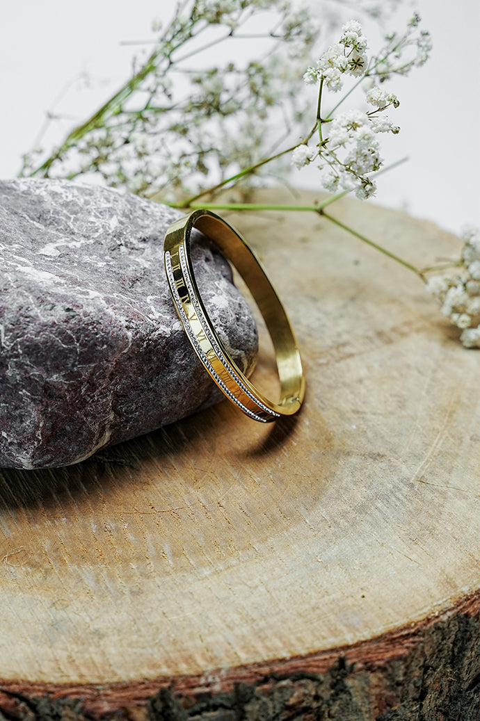 Gold Roman style bangle with rhinestone edge standing on a wooden slice