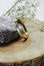 Gold Roman style bangle with rhinestone edge standing on a wooden slice