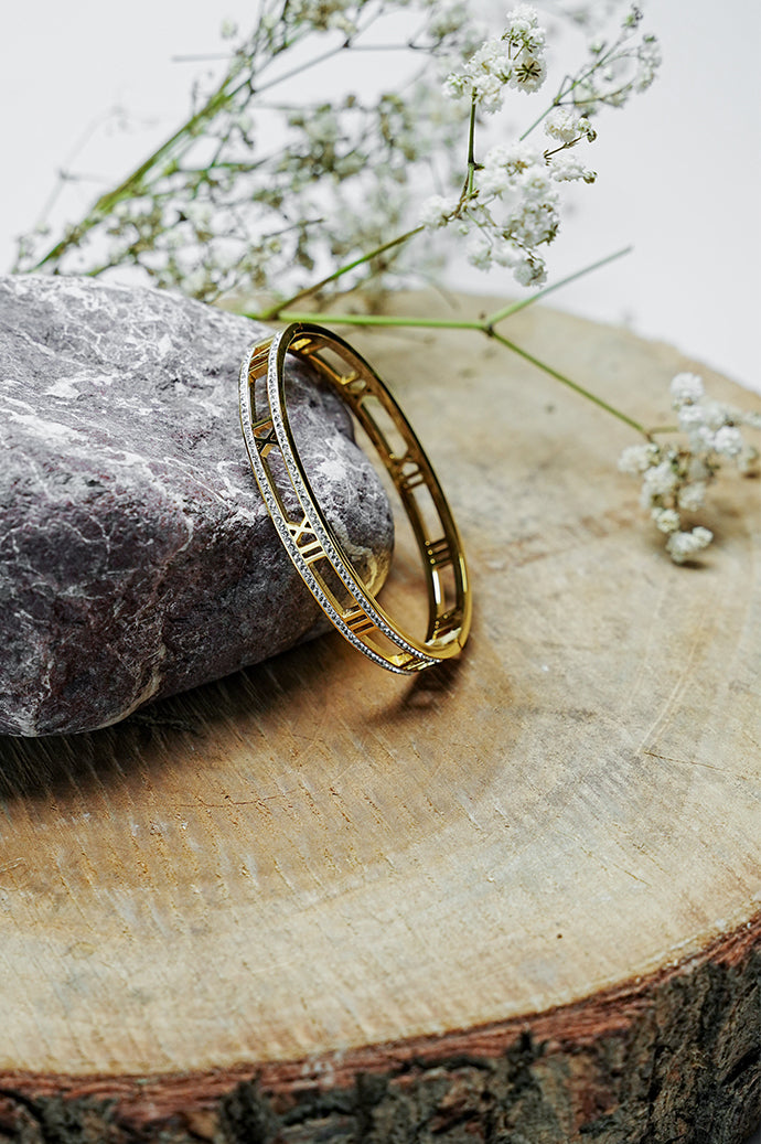 Gold Roman style bangle with rhinestones standing on a wooden slice
